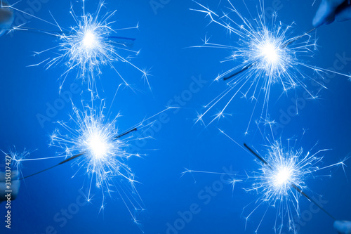 Close up of Bright burning four sparklers in hands on a blue background. © esvetleishaya