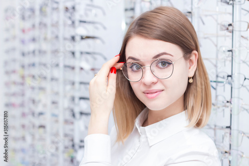 healthcare, people, vision and vision concept. Girl smiling trying on glasses in the store.