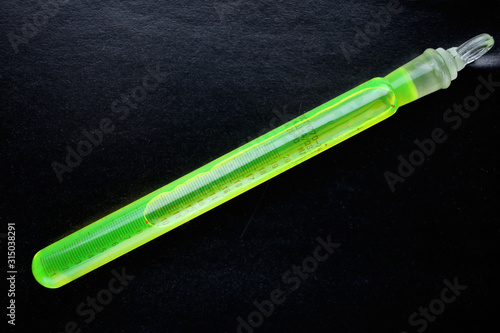 Volumetric test tube with a green fluorescent dye fluorescein, on a black background.