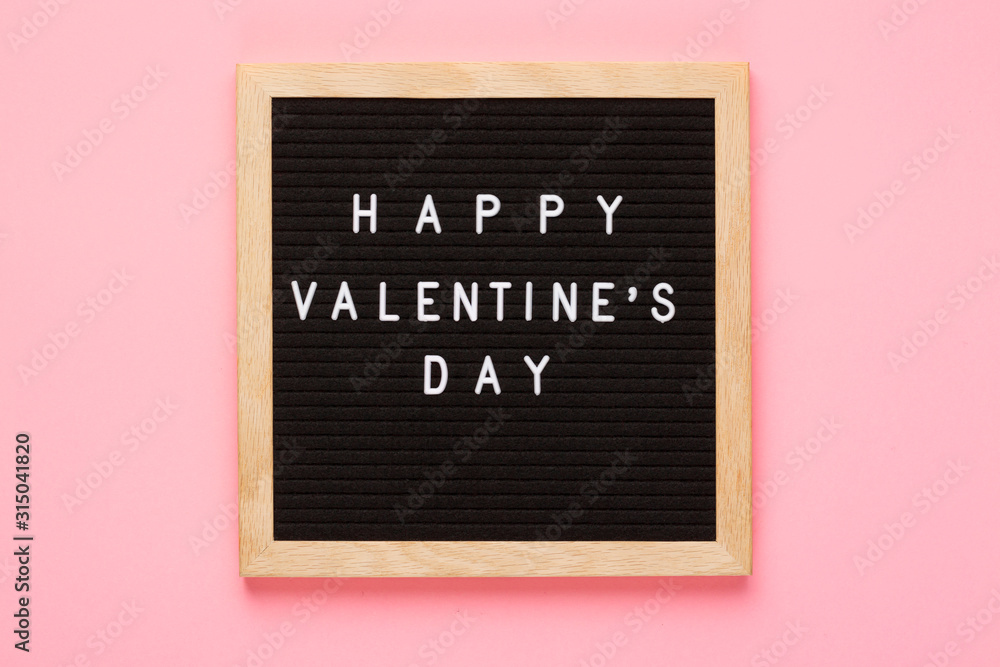 Fototapeta Valentines Day concept mockup. Happy Valentines day words on black letter board with wooden frame on pink background.