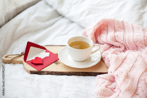 Beautiful white cup with tea on the bed, pink knitted plaid, postcard Happy Valentine's Day. Breakfast in bed. Morning. Spring. Cozy.