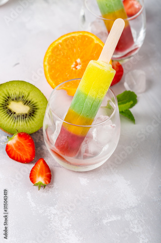 Delicious homemade popsicle with different flavors  mango  orange  kiwi and strawberry in glass cups. Summer food concept with copy space.