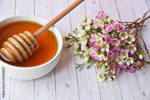 Pink and white manuka flower and honey in a white bowl and dipper in it