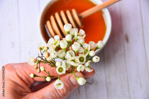 Pink and white manuka flower and honey in a white bowl and dipper in it