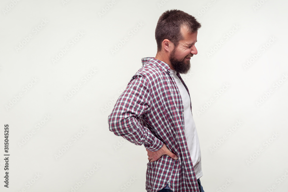 Portrait of unhealthy bearded man in casual plaid shirt touching sore back feeling backpain, pinched nerve aching lower spine, kidney inflammation. indoor studio shot isolated on white background Portrait of unhealthy bearded man in casual plaid shirt touching sore back feeling backpain, pinched nerve aching lower spine, kidney inflammation. indoor studio shot isolated on white background