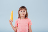  little girl has a corn in her hand. isolated on blue background, copy space, in studio, profile view