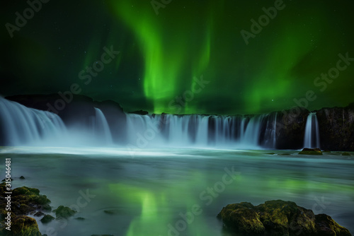 A magnificent night view of the cascades of the waterfall and the northern lights. Iceland. Long exposure.