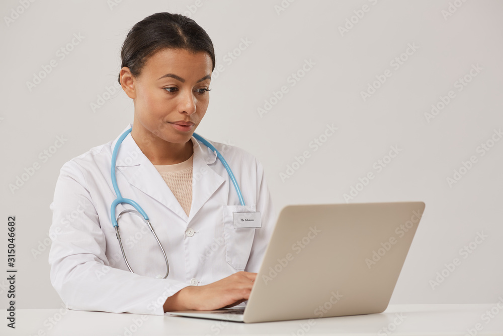 Portrait of beautiful female doctor using laptop while sitting against white background, copy space Portrait of beautiful female doctor using laptop while sitting against white background, copy space