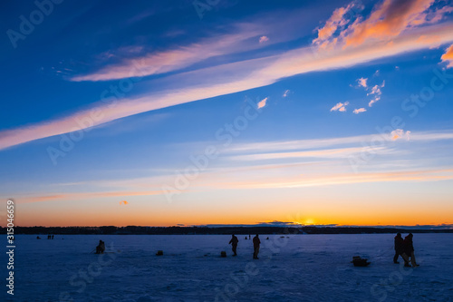 silhouettes of male fishermen on winter fishing on the ice of the river © alexkoral