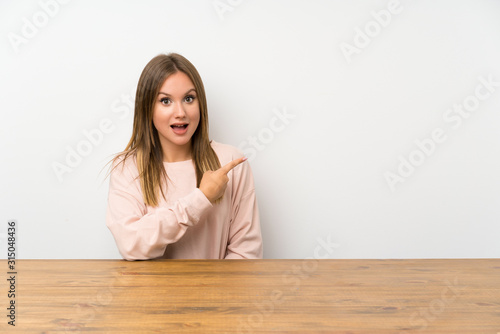 Teenager girl in a table pointing finger to the side