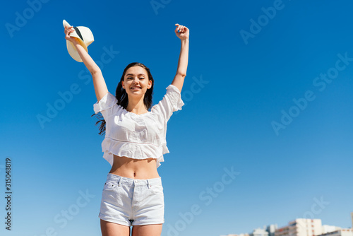 a girl with an emotion of sincere joy on her face triumphantly threw both hands up against the blue sky