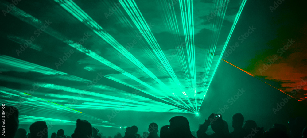  colorful outdoor laser show with silhouette of people - obrazy, fototapety, plakaty 