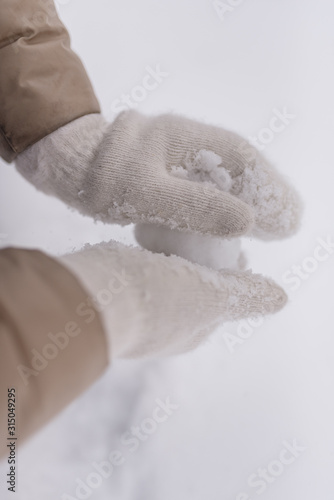 Woman makes a snowball in the hands of white mittens