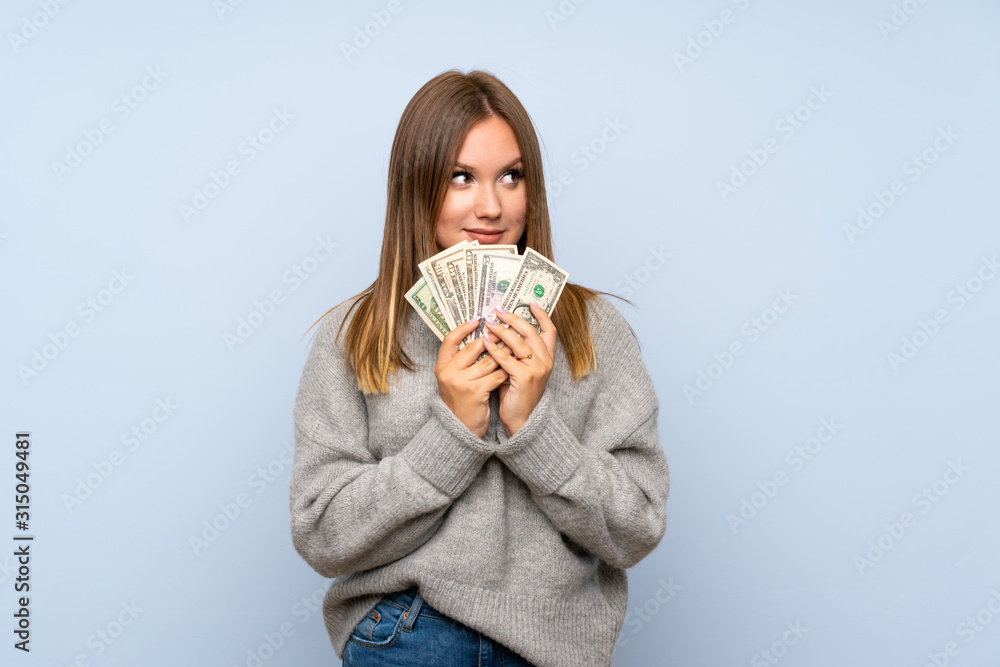 Teenager girl with sweater over isolated blue background taking a lot of money Teenager girl with sweater over isolated blue background taking a lot of money
