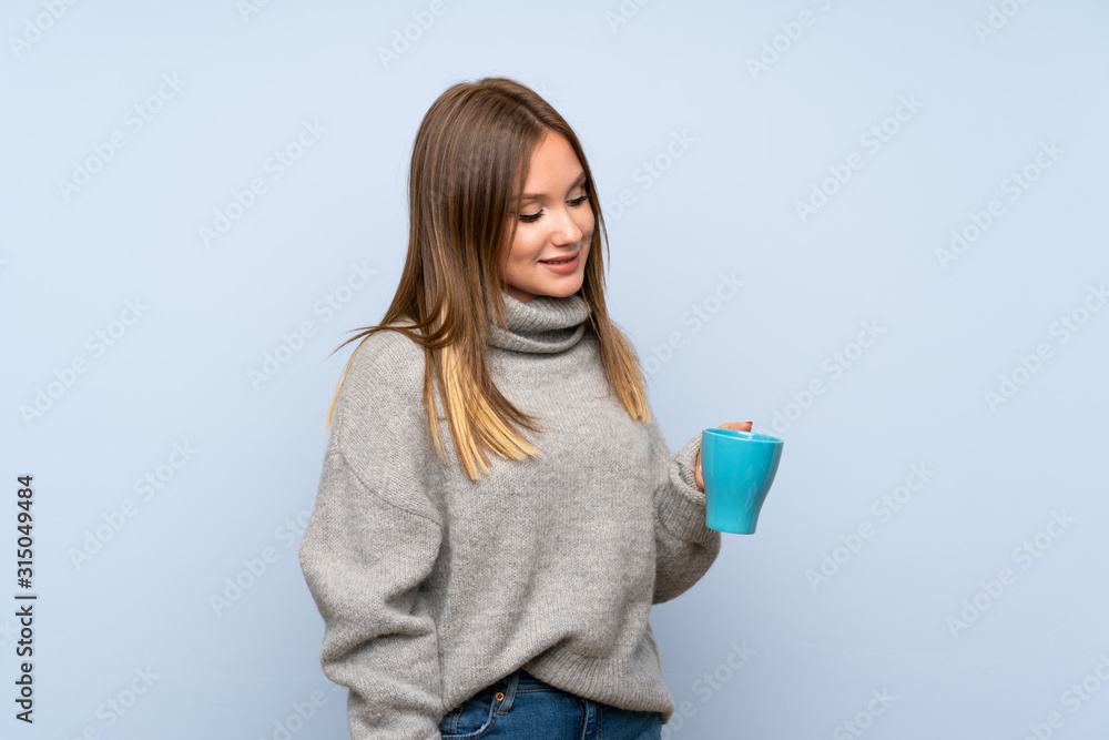 Teenager girl with sweater over isolated blue background holding hot cup of coffee Teenager girl with sweater over isolated blue background holding hot cup of coffee