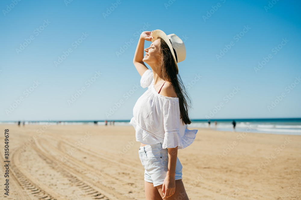 girl looking up at the sky standing on a sandy beach, people are walking far from the ocean
