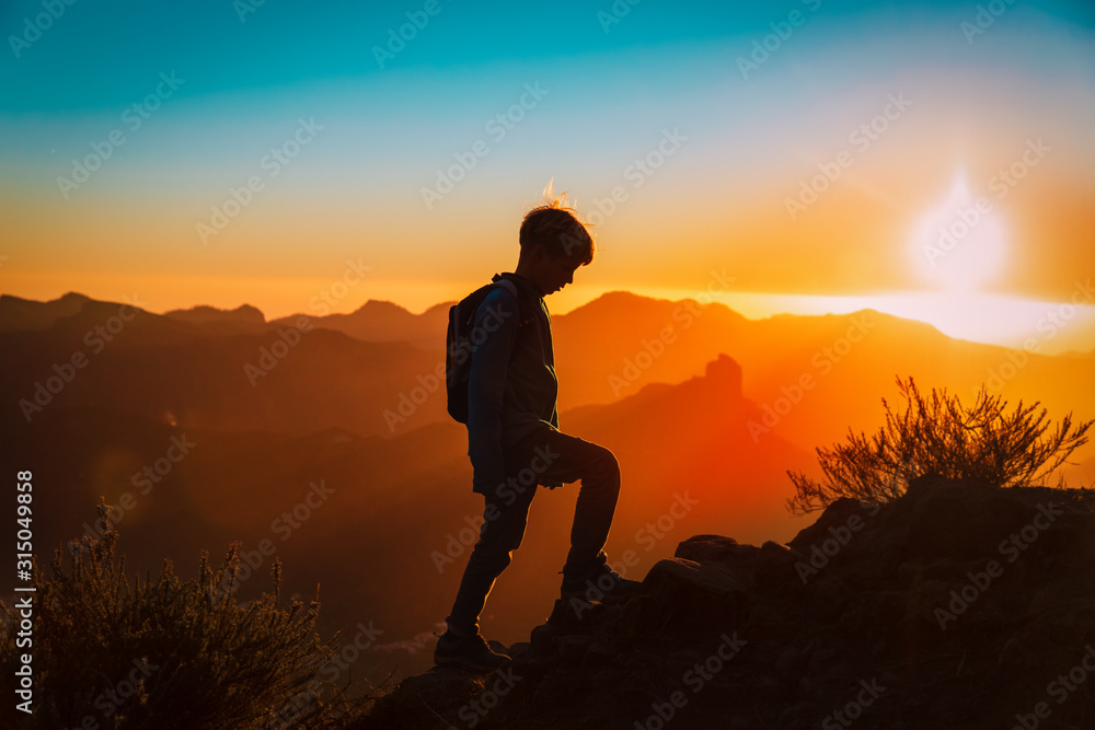Silhouettes of young boy hiking at sunset mountains