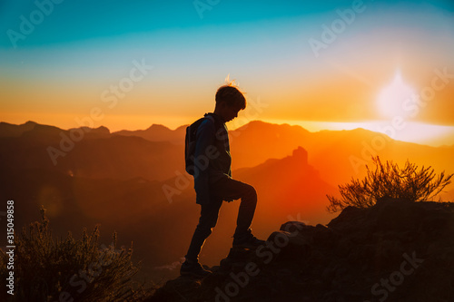 Silhouettes of young boy hiking at sunset mountains