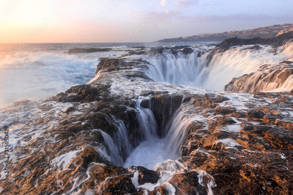 Olas batiendo en dos agujeros formados en las rocas al amanecer. Impresionante formación rocosa en Gran Canaria