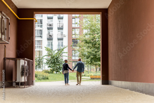 back view of mature man and woman holding hands and walking near new houses © LIGHTFIELD STUDIOS