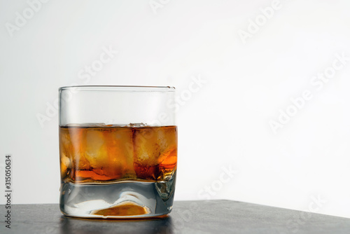 Glass of aged golden whiskey with ice cubes on the table. Amber colored alcohol beverage with rocks at the bar