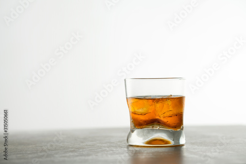 Glass of aged golden whiskey with ice cubes on the table. Amber colored alcohol beverage with rocks at the bar