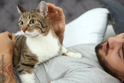 Man with cat on bed at home, closeup. Friendly pet
