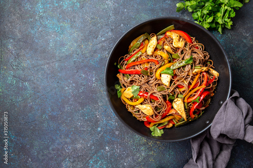 Japanese dish buckwheat soba noodles with chicken and vegetables carrot, bell pepper and green beans in wok on dark blue background