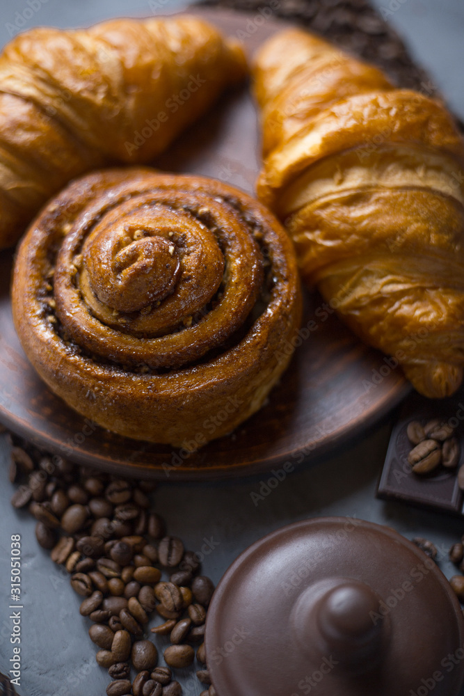 Fototapeta premium Croissants and a bun are lying on a large plate; next to them is a lid for pigs on a table