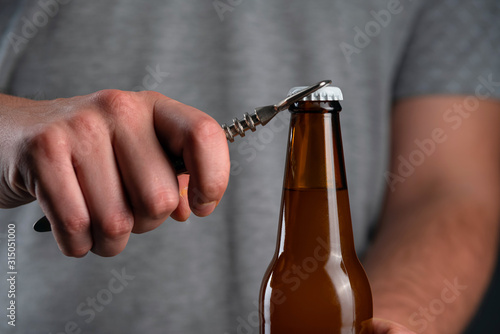 Men opening cold bottle of beer with cap on black background. Hands cracking refrigerated wheat or lager beer with an opener on dark background
