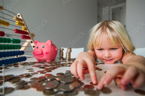 child counting coins and saving money, cute girl put coins into piggy bank