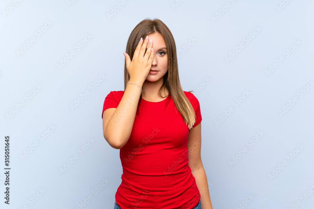 Teenager girl over isolated blue background covering a eye by hand Teenager girl over isolated blue background covering a eye by hand