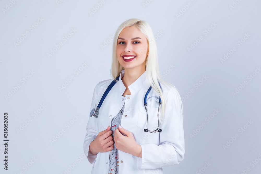 Medical concept of beautiful female doctor in white coat with phonendoscope. Medical student general practitioner. Woman hospital worker looking at camera and smiling, studio, gray background Medical concept of beautiful female doctor in white coat with phonendoscope. Medical student general practitioner. Woman hospital worker looking at camera and smiling, studio, gray background