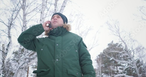 A man in winter in forest dialing a phone number and smiling. Talking
