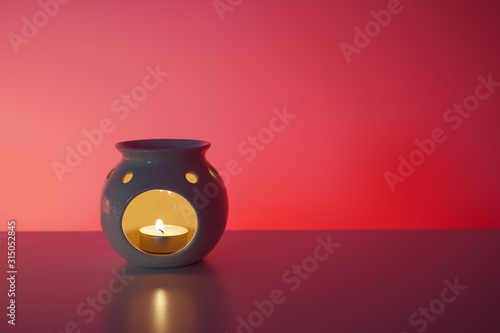 Aroma lamp with burning candle, reflection, red background. Relax, spa, healthcare concept. Close-up, copy space