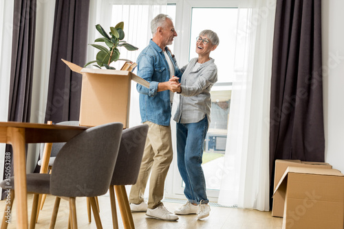 mature man and smiling woman dancing in new house