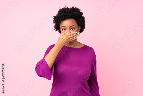 African american woman over isolated pink background covering mouth with hands