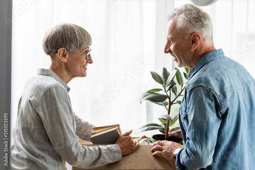 side view of smiling man and mature woman unpacking box in new house