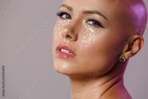 Portrait of gorgeous young half-naked bald woman with glitter face