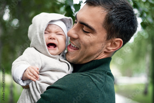smiling dad with crying baby in his arms in the Park © Руслан Галиуллин