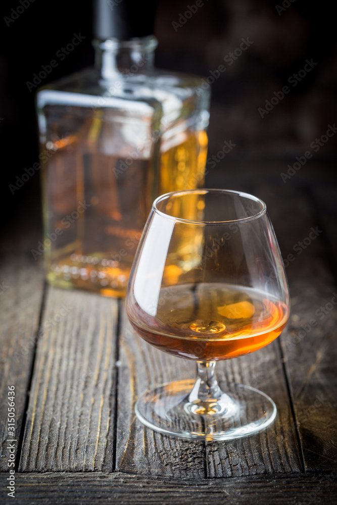 Glass and a bottle of brandy or cognac on the wooden table. Glass and a bottle of brandy or cognac on the wooden table.