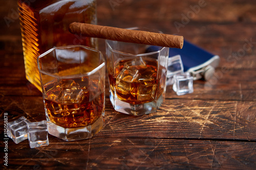 Bottle of whiskey with two glasses and cuban cigar placed on rustic wooden table © Dash