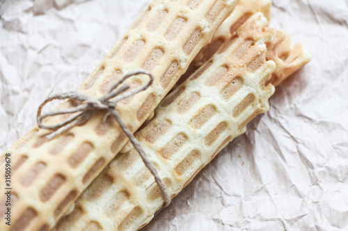 Homemade wafer rolls tied with jute on baking paper background. Close-up photo, space for text.