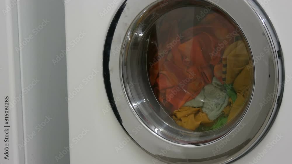 Multi-colored clothes laundry is washed in a white washing machine in the laundry room Multi-colored clothes laundry is washed in a white washing machine in the laundry room