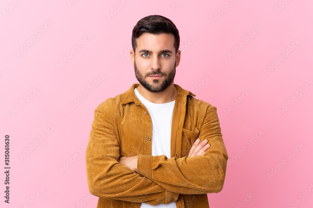 Young handsome man with beard wearing a corduroy jacket over pink background keeping arms crossed Young handsome man with beard wearing a corduroy jacket over pink background keeping arms crossed