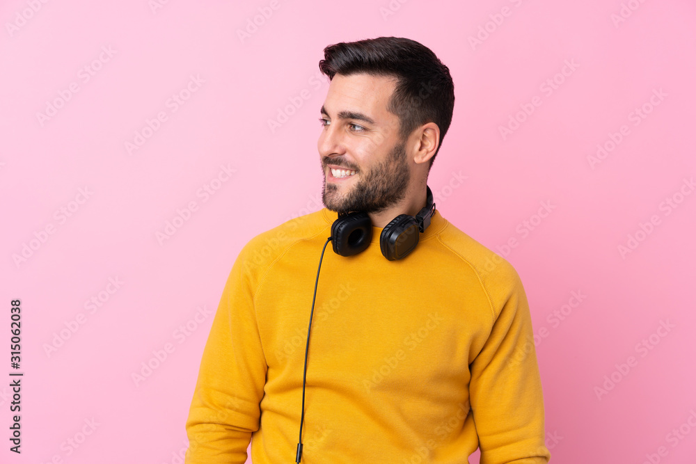 Young handsome man with earphones over isolated pink background looking side Young handsome man with earphones over isolated pink background looking side