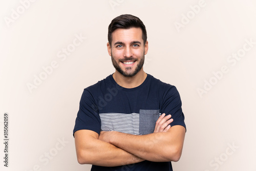 Young handsome man with beard over isolated background keeping the arms crossed in frontal position