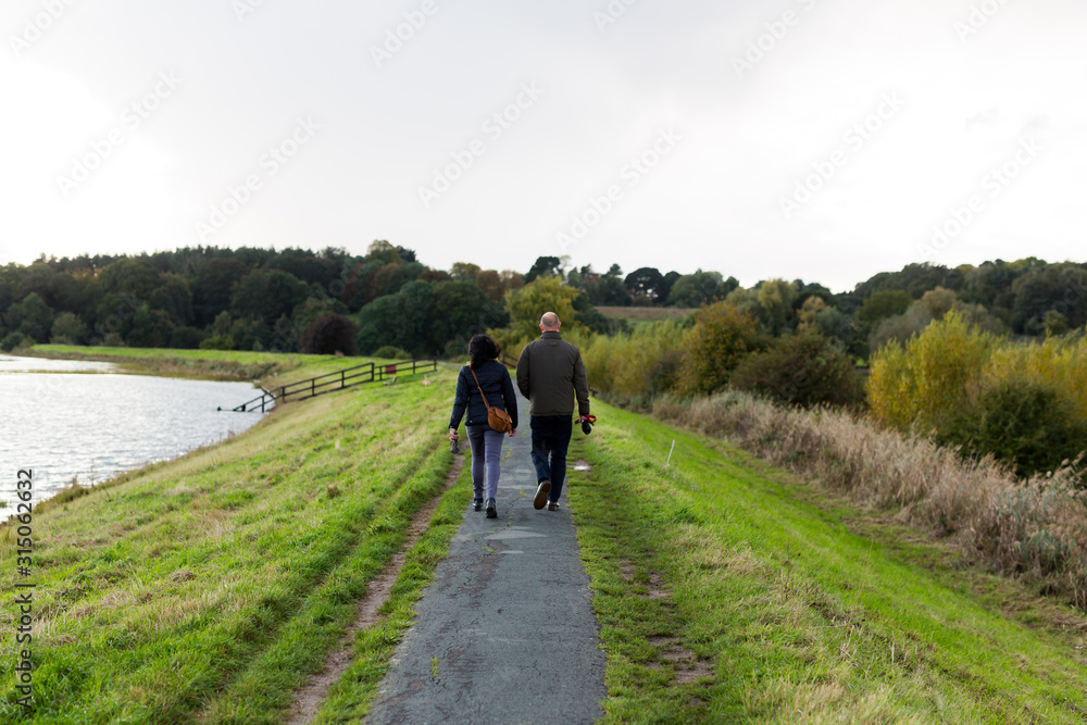 A middle aged couple taking a walk along a river path on a dull autumn afternoon A middle aged couple taking a walk along a river path on a dull autumn afternoon