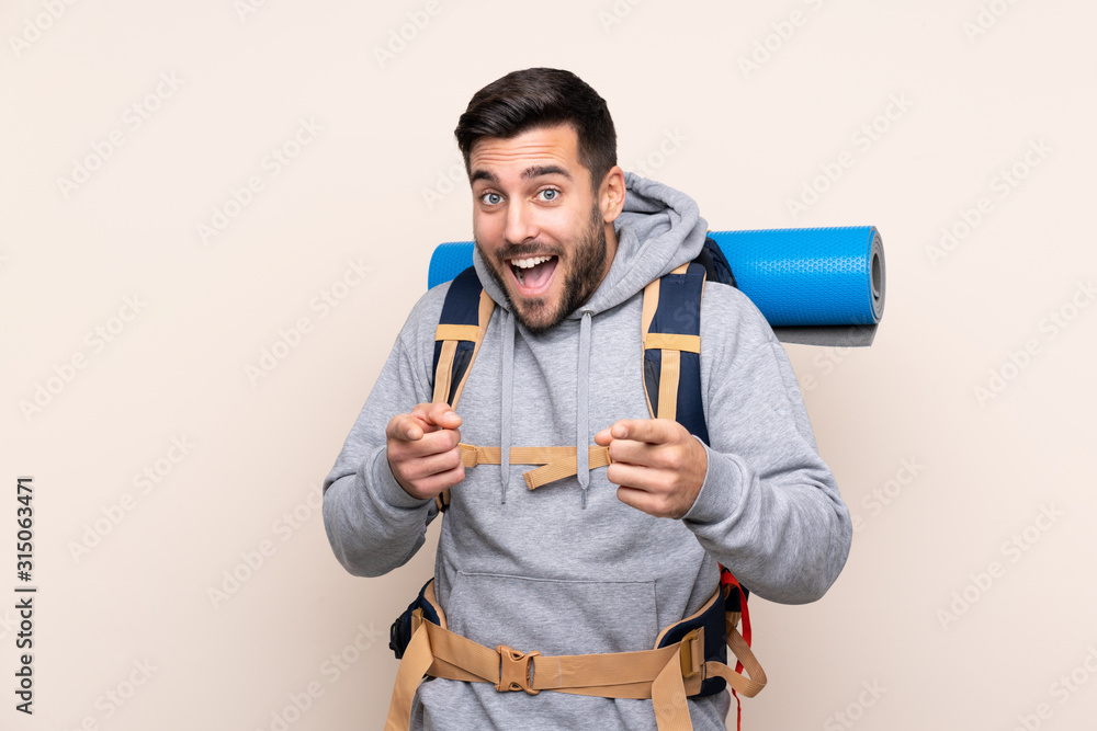 Young mountaineer man with a big backpack over isolated background points finger at you Young mountaineer man with a big backpack over isolated background points finger at you