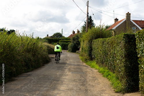 Man riding a bike down a rural country lane. He is wearing high vis and a helmet for safety